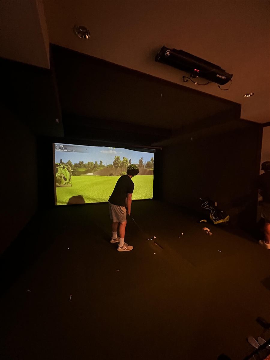 Een speler slaat af voor het grote scherm van de golfsimulator